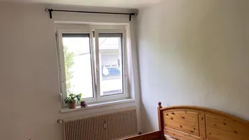 Helles Schlafzimmer mit Holzbettrahmen, Laminatboden und einem Fenster für natürliches Licht.