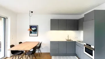 Moderne offene Küche mit grauen Schränken, Holztisch und Zugang zum Außenbereich.