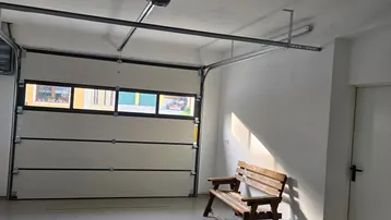Helle und saubere Garage mit automatischem Sektionaltor, Betonboden und einer Holzsitzbank.
