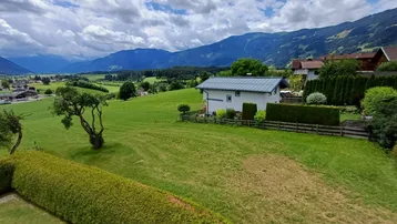 Panoramablick auf ein Haus in einer grünen Hügellandschaft mit majestätischen Bergen im Hintergrund.