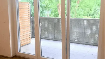 Heller Raum mit Holzboden und großer Schiebetür, die auf einen Balkon führt.