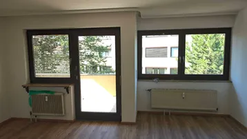 Helles Zimmer mit Laminatboden, weißen Wänden und Zugang zu einem Balkon.