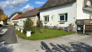 Außenansicht eines Hauses mit kleinem Vorgarten und Zufahrt an einem sonnigen Tag.