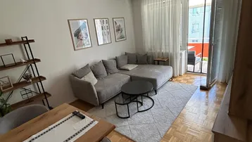 Heller Wohn- und Essbereich mit modernem Sofa, Holztisch und Zugang zu einem Balkon.