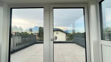 Blick aus dem Innenraum auf eine weitläufige Dachterrasse mit beeindruckendem Bergblick.