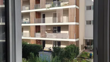 Blick aus dem Fenster auf ein modernes Wohngebäude mit Balkonen und begrüntem Innenhof.
