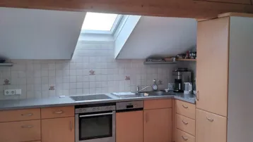 Helle Küche im Dachgeschoss mit Holzbalken, Dachfenster und funktionalen Einbauschränken.
