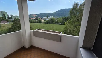 Heller Balkon mit Fliesenboden und weitem Blick ins Grüne und auf die Berge.