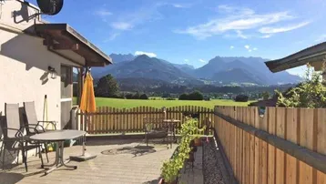 Große gepflasterte Terrasse mit Sitzgelegenheiten und einem weiten Blick auf die umliegende Berglandschaft.
