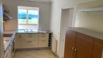 Funktionale Küche mit hellen Schränken, Fliesenboden und einem Fenster mit Blick ins Grüne.