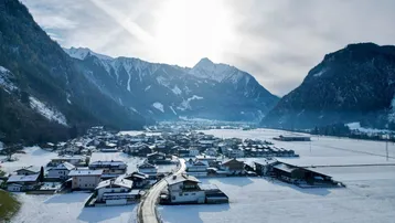 Weitläufige Luftaufnahme eines verschneiten Dorfes in einem Tal, umgeben von majestätischen Bergen.