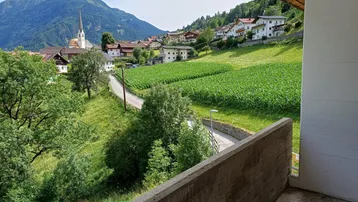 Balkon mit weitem Blick auf eine ländliche Landschaft, Berge und ein Dorf mit Kirche.