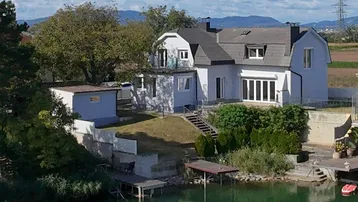 Panoramablick auf das Haus am See mit Bootsstegen und umliegender Natur.