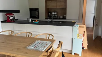 Helle, moderne Küche mit Kochinsel, Holztisch und integrierten Geräten für Familienleben.