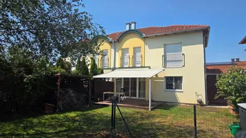 Hinterhof mit Rasenfläche, Terrasse und einem kleinen Gartenhaus unter blauem Himmel.