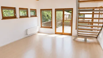 Helles Wohnzimmer mit Holzbalkendecke, Laminatboden und Zugang zu einer Terrasse.