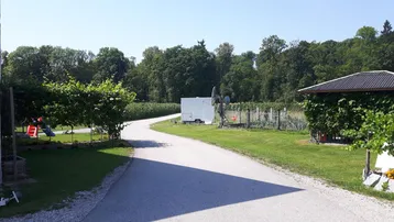 Ländliche Außenansicht mit Schotterweg, viel Grün und einem kleinen Spielplatz im Hintergrund.