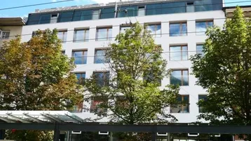 Modernes Gebäude mit vielen Fenstern und Bäumen davor in städtischer Umgebung.