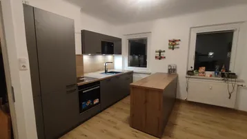 Moderne Küche mit dunklen Schränken, Holzarbeitsplatten und integrierten Geräten, gut beleuchtet.