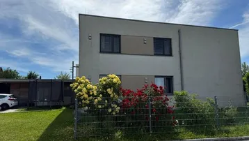 Modernes Gebäude mit schlichter Fassade, umgeben von einem kleinen Garten mit blühenden Rosen.
