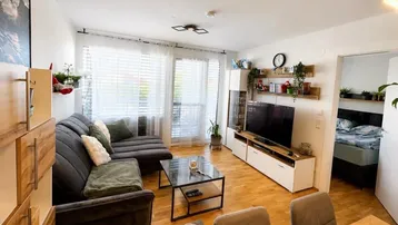 Helles Wohnzimmer mit modernem Sofa, TV-Möbel und Zugang zu einem Balkon.