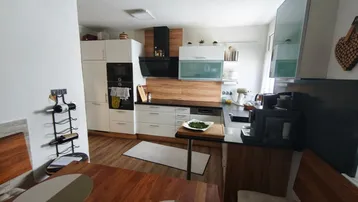 Moderne Küche mit weißen Schränken, Holzakzenten und integriertem Essbereich mit Holztisch und Bänken.