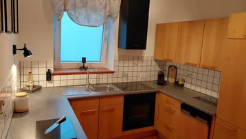 Funktionale Küche mit hellen Holzschränken, Induktionskochfeld, Backofen und Spülmaschine.