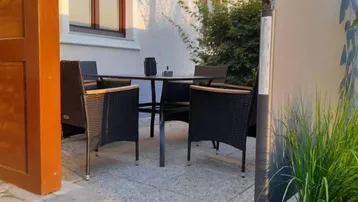Gemütlicher Außenbereich mit schwarzem Tisch und Stühlen, umgeben von Pflanzen.