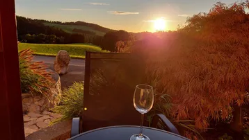 Sonnenuntergang über der Landschaft, genossen von einer gemütlichen Terrasse mit Weinglas.