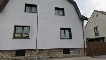 Weiß verputztes Wohnhaus mit Satteldach und Steinsockel, umgeben von einer ruhigen Wohngegend.