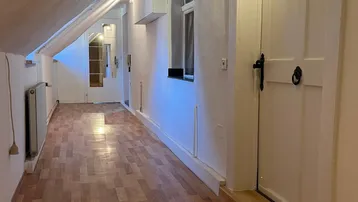 Langer Flur im Dachgeschoss mit schrägen Wänden, Holzfußboden und Fenstern, die für Helligkeit sorgen.