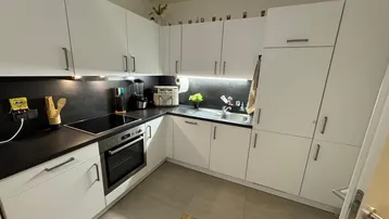 Moderne Küche mit weißen Schränken, dunkler Arbeitsplatte und integrierten Geräten, gut beleuchtet.