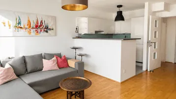 Helles Wohnzimmer mit offener Küche, bequemer Couch und modernem Segelbild an der Wand.