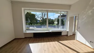 Helles Wohnzimmer mit großen Fenstern, Holzboden und Blick ins Grüne.
