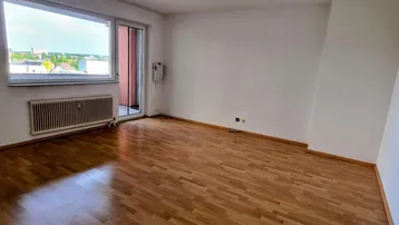 Helles Wohnzimmer mit Laminatboden und großem Fenster, das einen weiten Blick über die Umgebung bietet.
