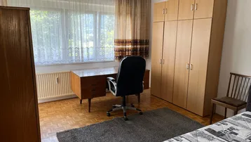 Helles Schlafzimmer mit Holzboden, großem Fenster und Blick ins Grüne, ausgestattet mit Schrank und Schreibtisch.