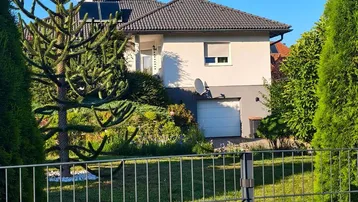 Ansicht eines Einfamilienhauses mit Gartenbereich und Garage unter blauem Himmel.