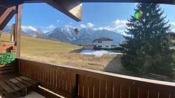 Balkon mit Holzboden und atemberaubendem Blick auf die schneebedeckten Berge und grüne Felder.