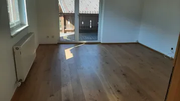 Helles Zimmer mit Holzboden und Zugang zu einem Balkon, ideal als Schlafzimmer nutzbar.