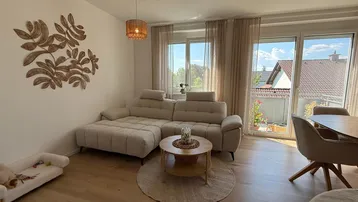 Helles Wohnzimmer mit beigem Ecksofa, Holzboden und Zugang zum Balkon.