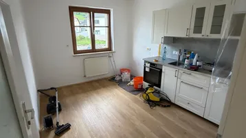 Kleine Küche mit weißer Einbauküche, Laminatboden und einem Fenster mit Tageslicht.