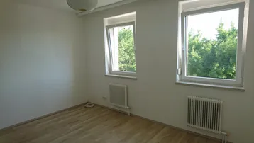 Helles Schlafzimmer mit Holzboden, zwei Fenstern und Blick ins Grüne.