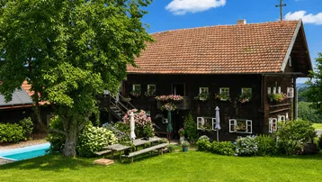 Traditionelles Holzhaus mit rotem Ziegeldach, umgeben von einem gepflegten Garten mit Pool und Sitzbereich.