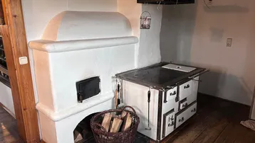 Traditionelle Küche mit weißem Kachelofen und einem Holzherd, bereit zum Kochen und Heizen.