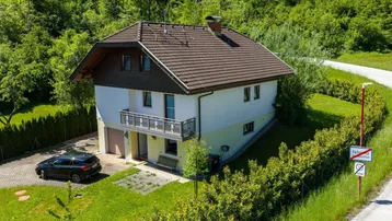 Freistehendes Einfamilienhaus mit Satteldach, Balkon und gepflegtem Gartenbereich, umgeben von viel Grün.