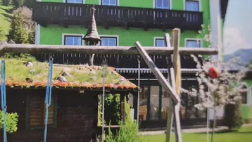 Grünes Gebäude im alpinen Stil mit Balkonen und einem Gartenbereich mit Schaukel und Hütte.