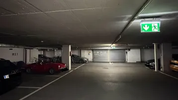 Geräumige Tiefgarage mit mehreren geparkten Fahrzeugen und einem grünen Notausgangsschild.