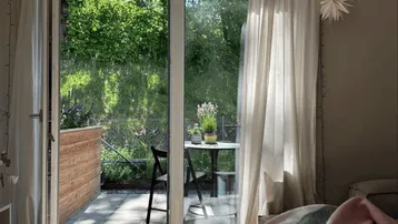 Helles Wohnzimmer mit Holzboden und direktem Zugang zu einem möblierten Balkon mit viel Grün.