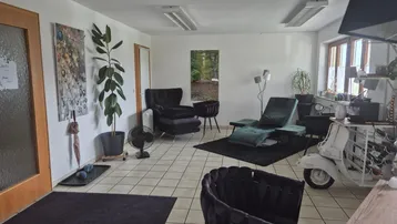 Geräumiger Innenraum mit beigen Fliesenboden, dunklen Lounge-Möbeln und einem Fenster mit grüner Aussicht.
