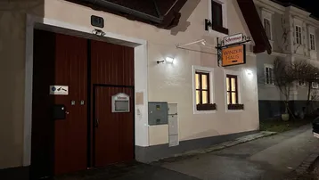 Fassade eines gepflegten Winzerhauses bei Nacht mit beleuchteten Fenstern und großem Tor.